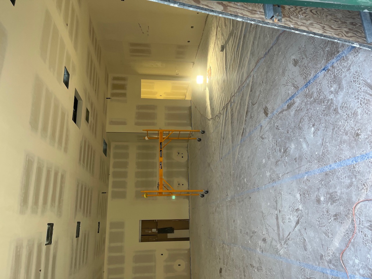 Barber shop space during remodel with fresh drywall taped and mudded, floors covered for paint prep