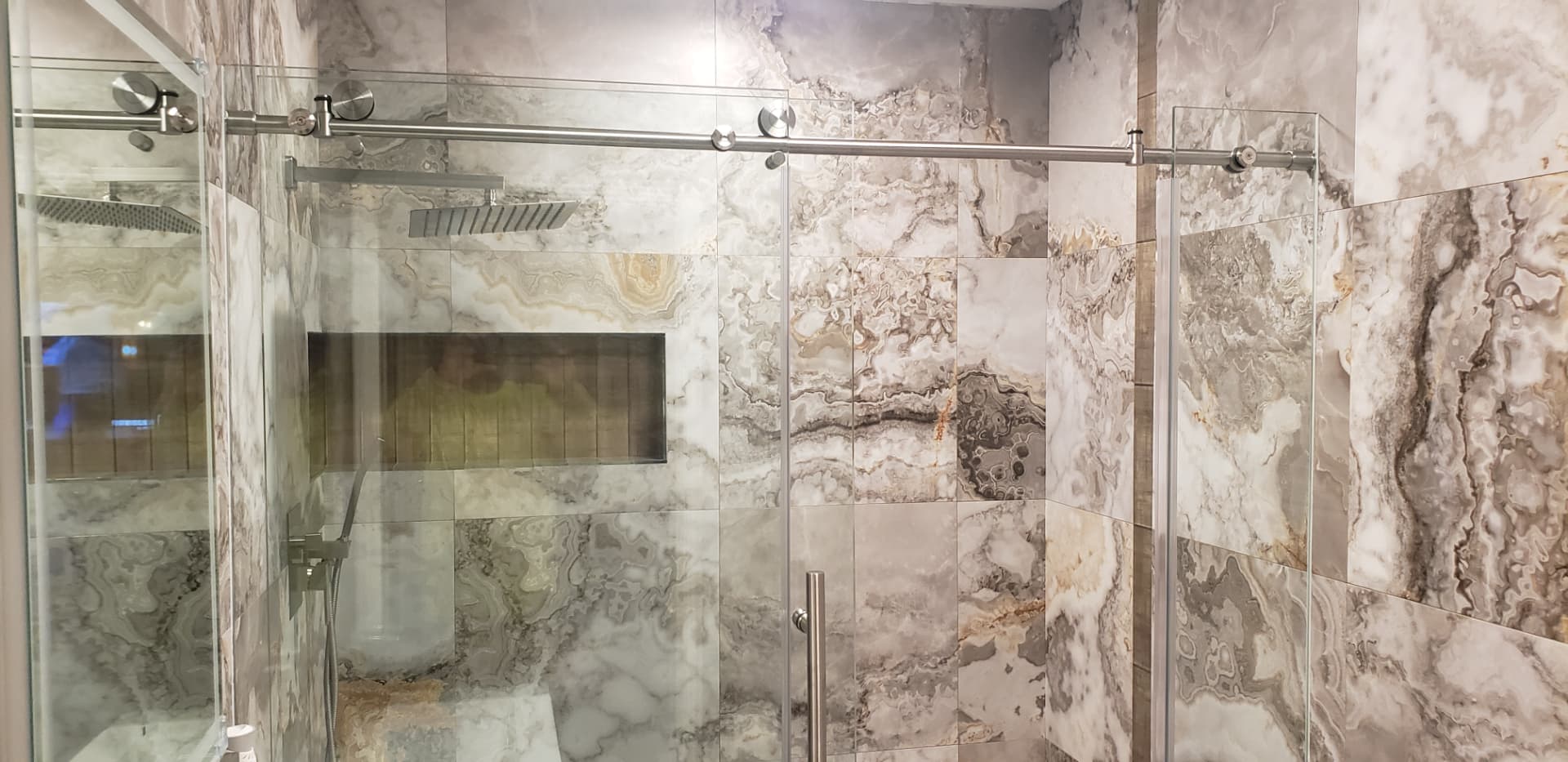 Remodeled walk-in shower with marble-look tile and frameless glass