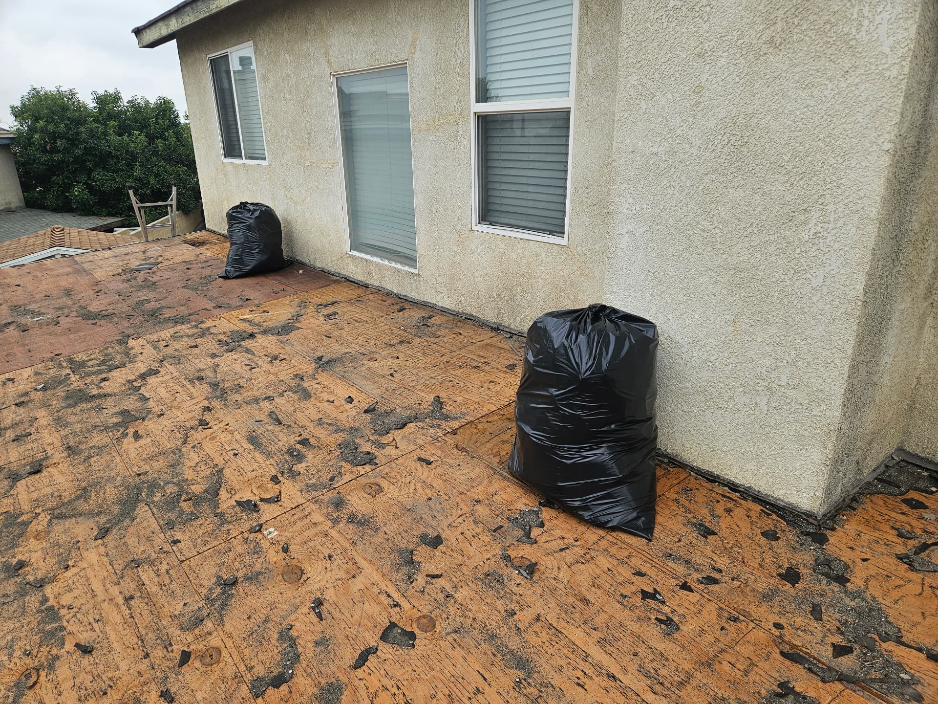 Low-slope deck roof stripped down to bare plywood sheathing with old shingles bagged for haul-off