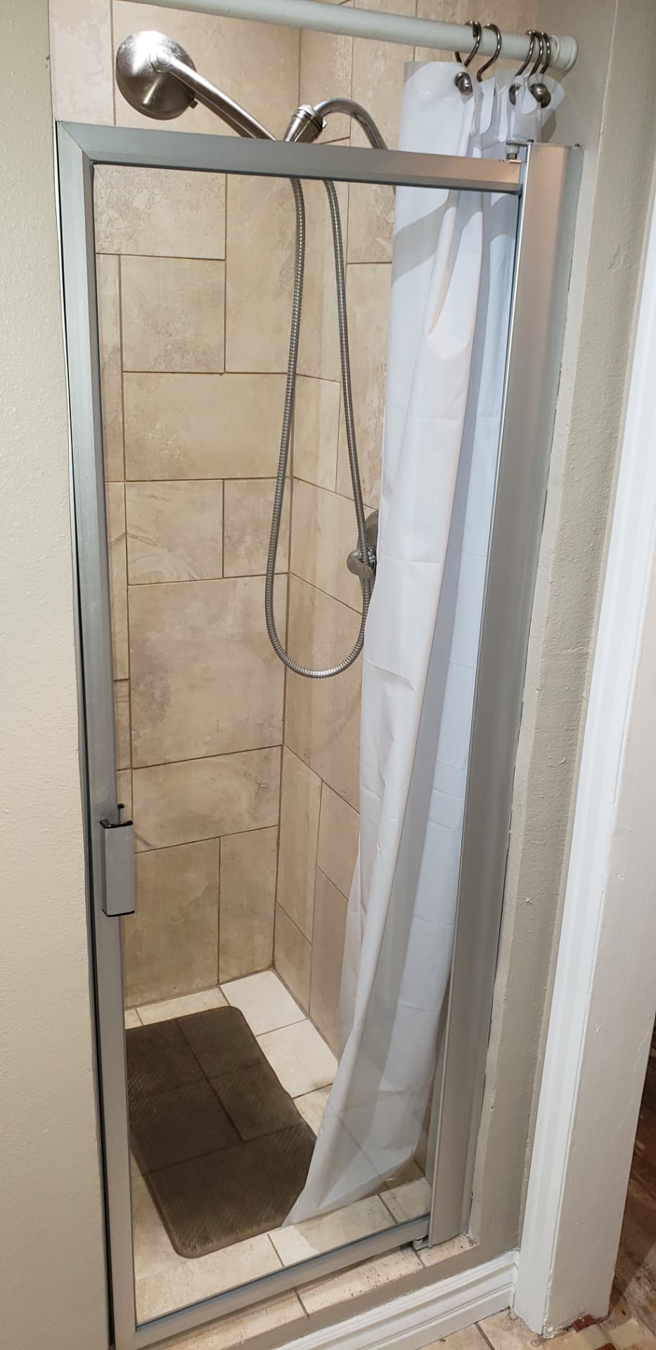 Dated shower with beige tile and framed glass door before remodel
