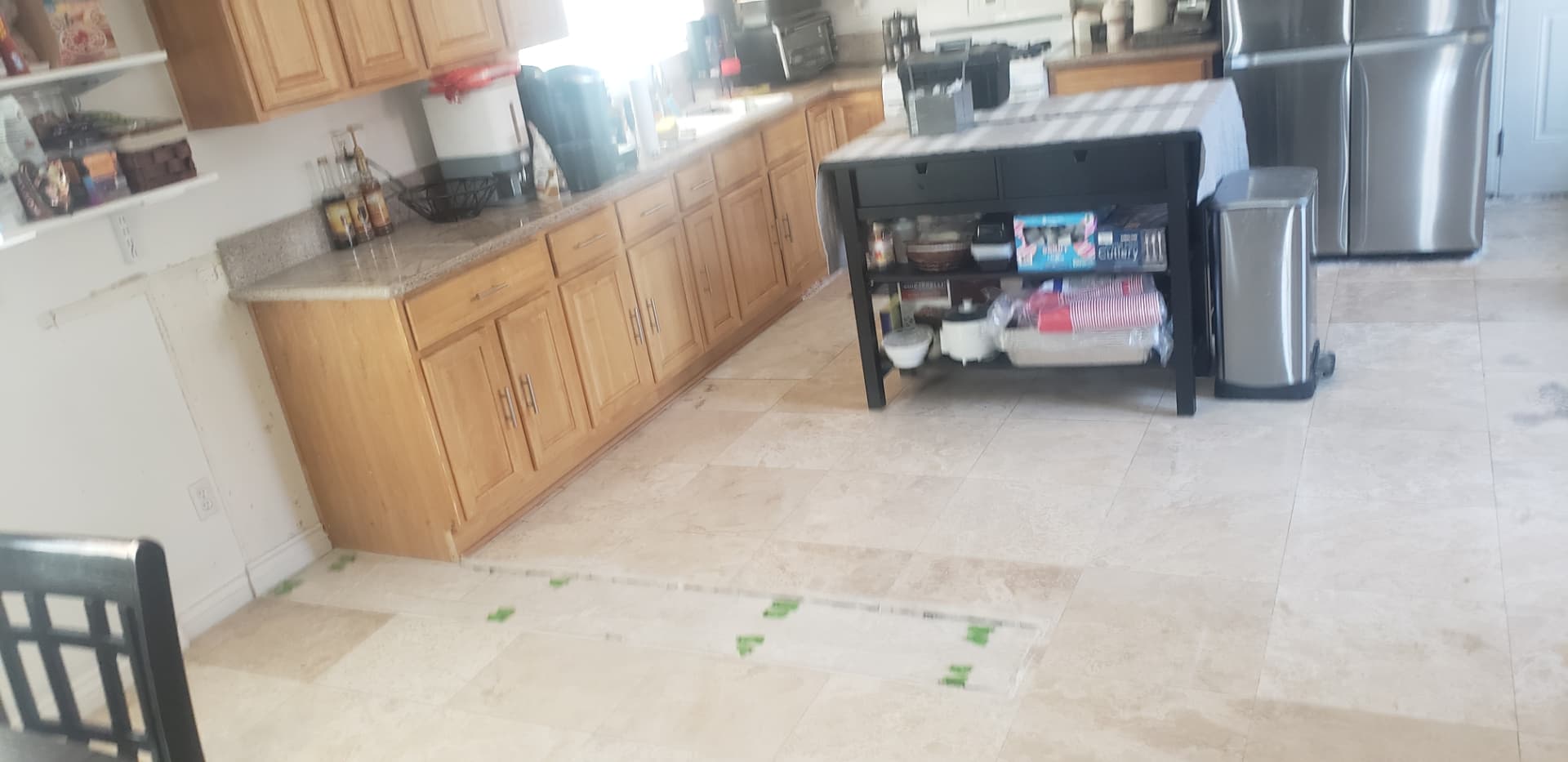 Kitchen with dated oak cabinets and a small rolling cart island, floor taped off for the new island layout