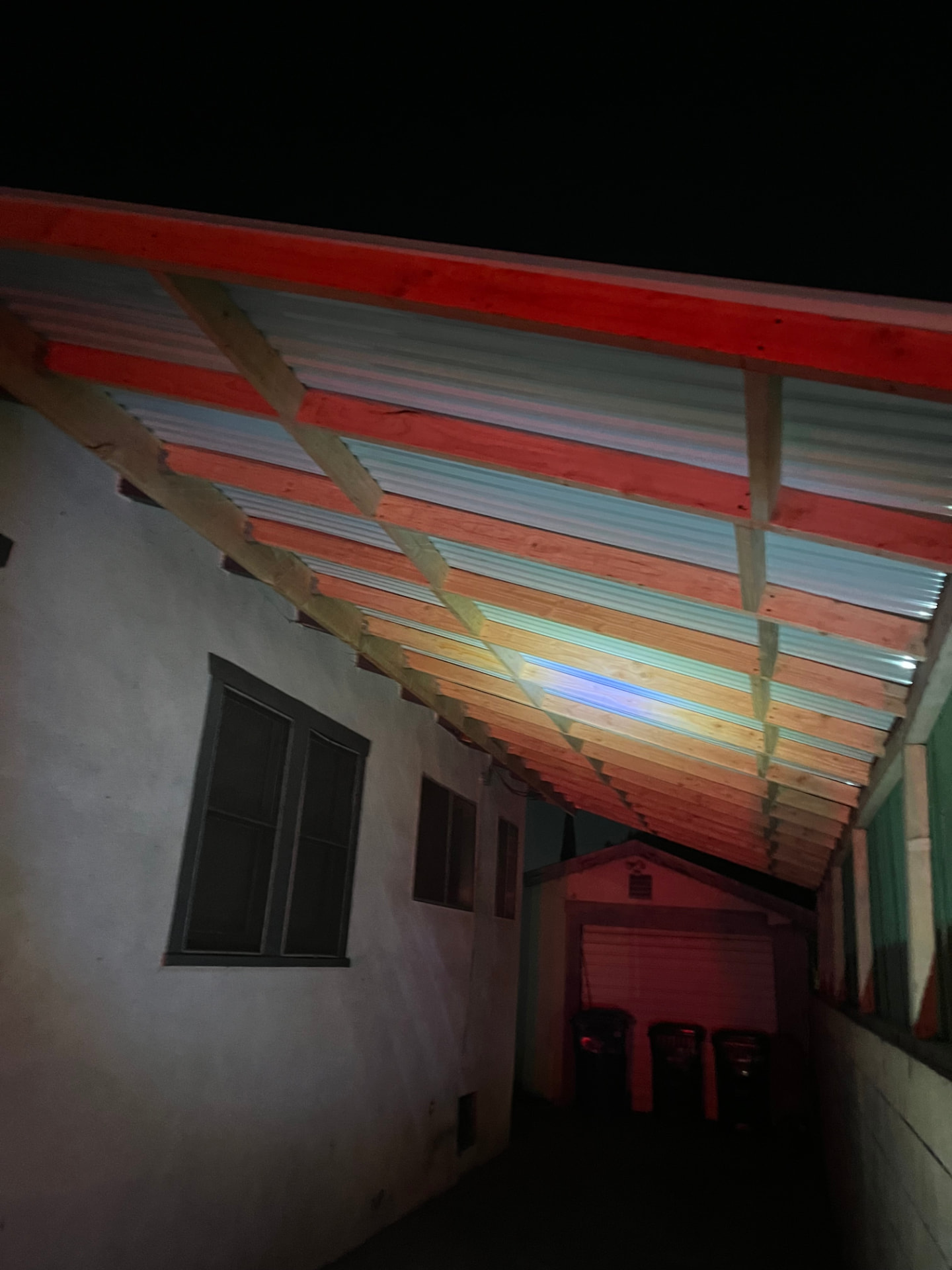 New side yard patio cover with wood rafters and translucent panels lit up at night