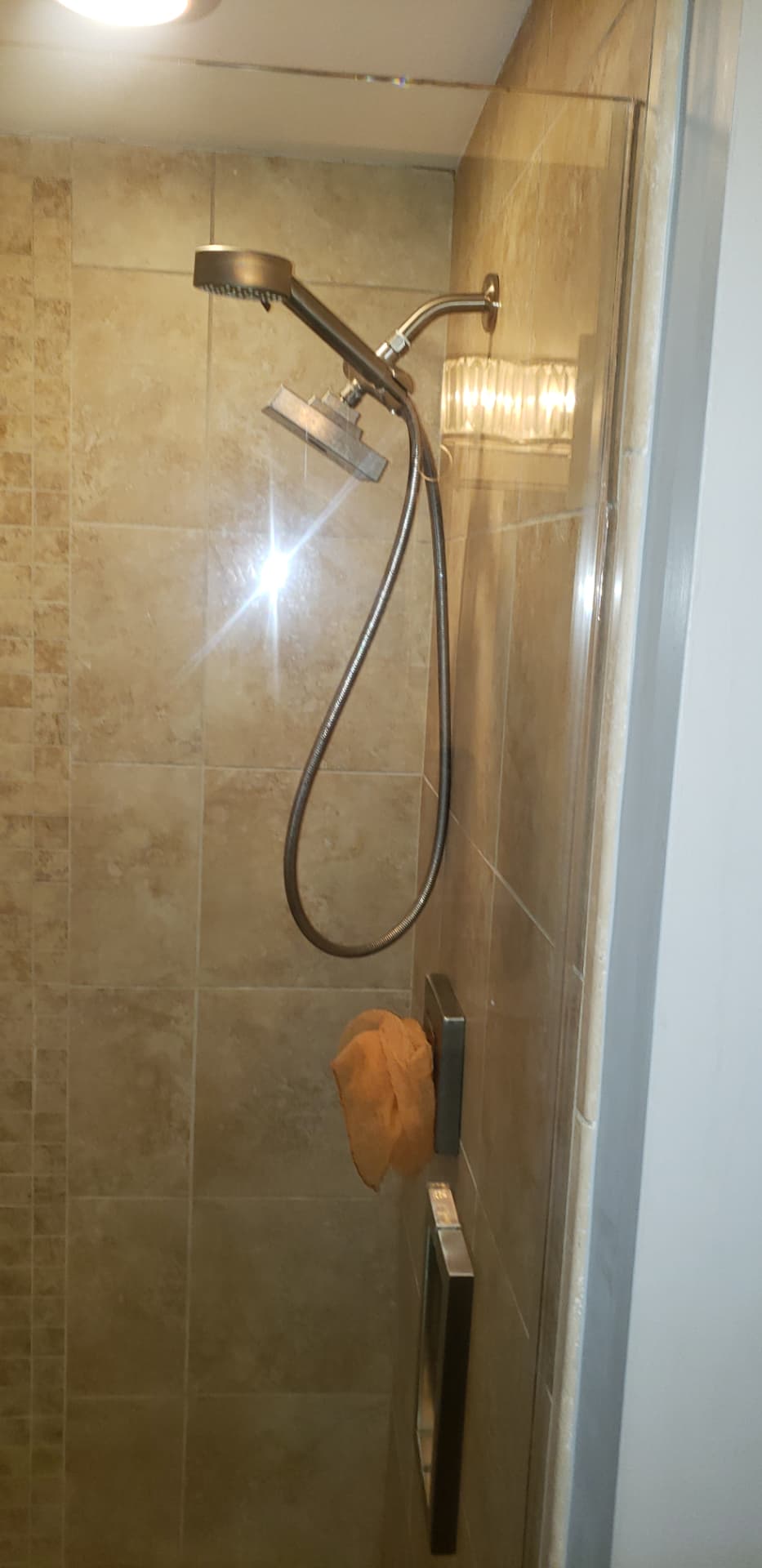 Original bathroom shower with dated beige travertine tile and a framed glass door