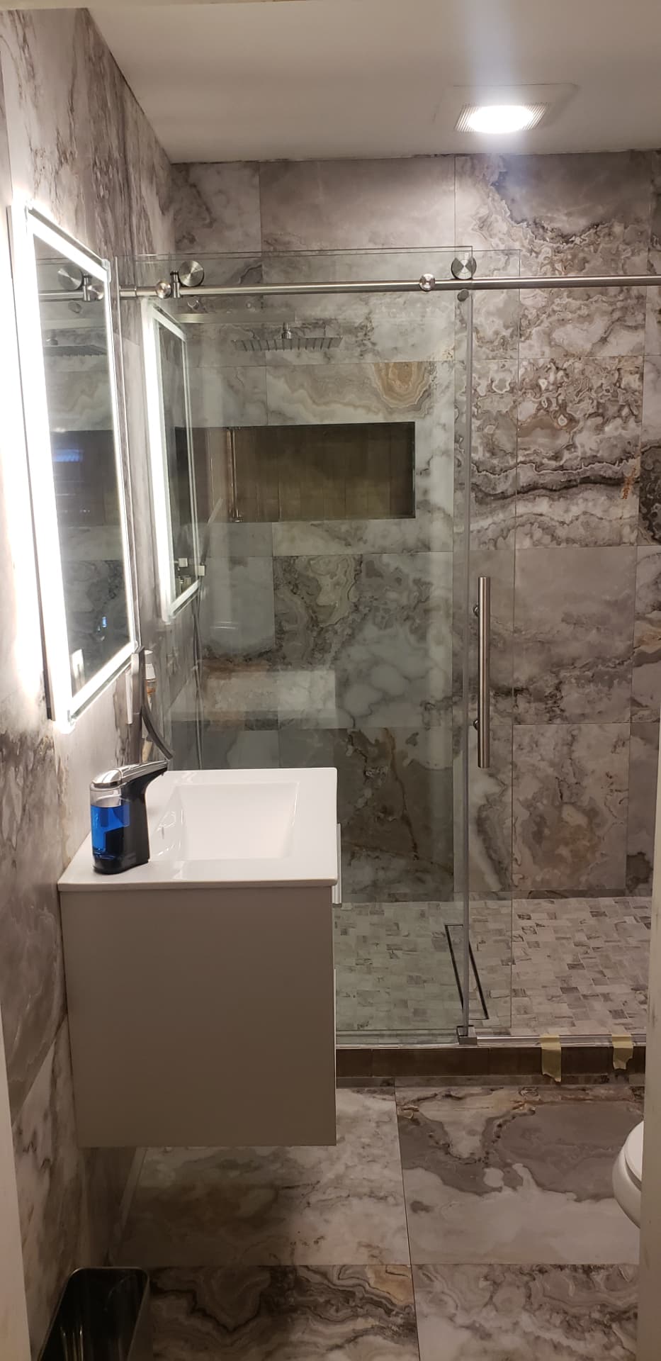 Remodeled bathroom with large-format marbled porcelain tile, frameless glass, floating vanity, and backlit mirror